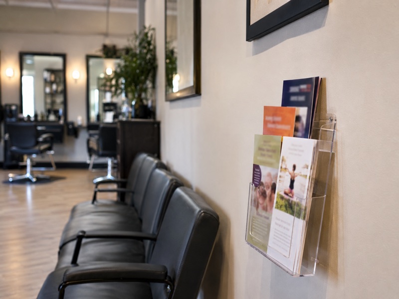 A wall-mounted flyer rack beside the waiting chairs in a salon